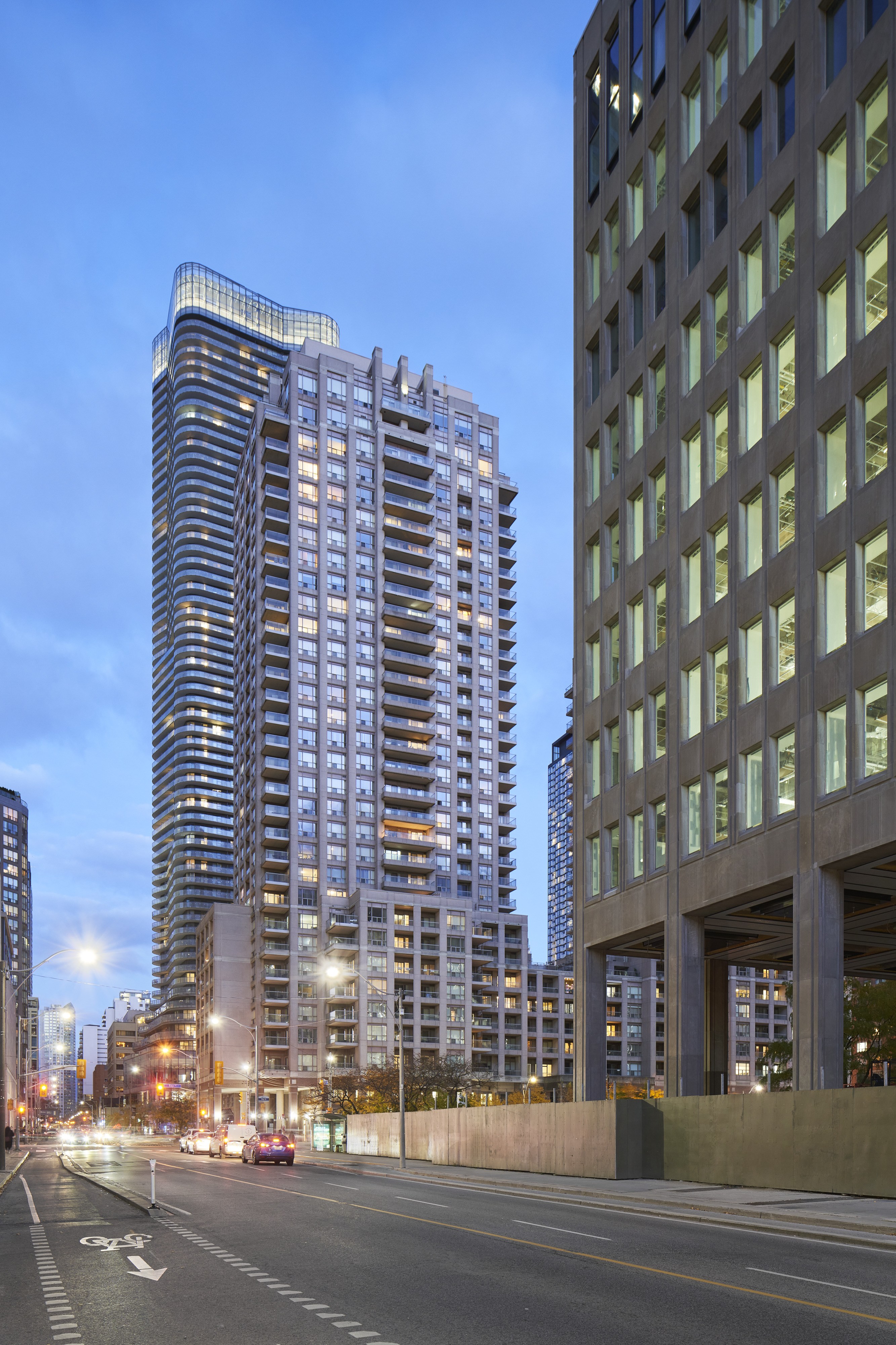 A tall building with a curved top stands next to a shorter building with a grid-like facade.